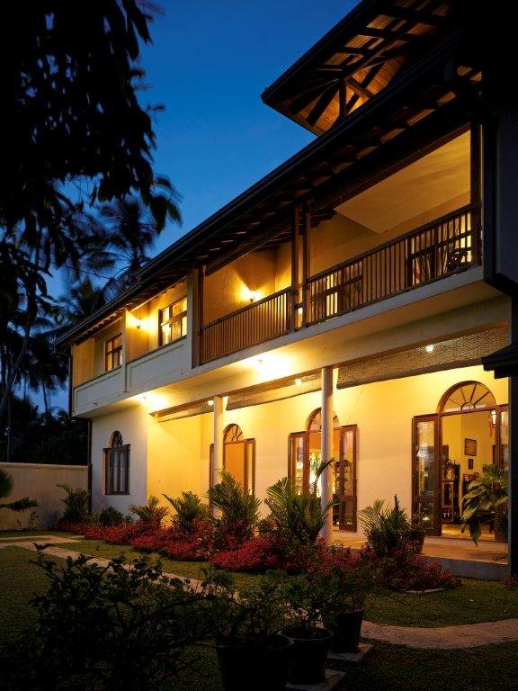 The villa from the garden at dusk, verandah lamps on
